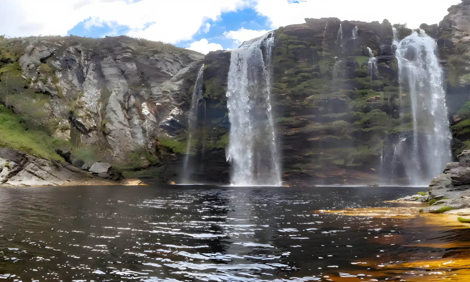 Cachoeira caindo de um paredão de pedra num poço de águas escuras, na região da Lapinha da Serra